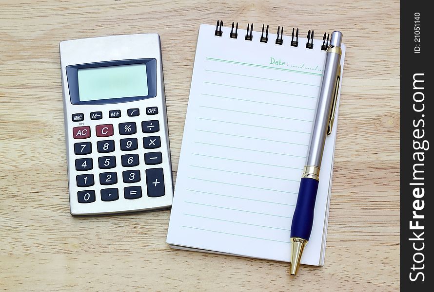 Notebook, silver ballpen and calculator on wooden desk