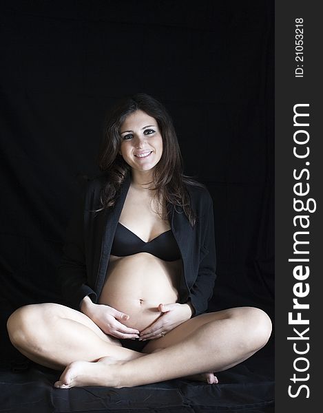 Pregnant woman sitting on a black background with a black robe. Pregnant woman sitting on a black background with a black robe