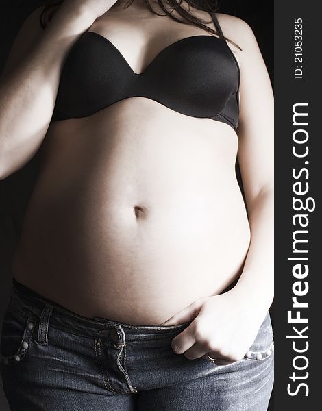 Big belly pregnant woman in jeans and black bra on a black background. Big belly pregnant woman in jeans and black bra on a black background