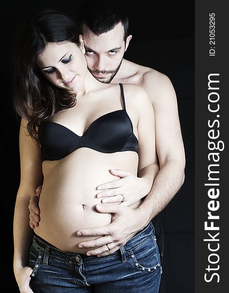 Happy pregnant women and father on black background caressing the belly with sweetness, love and protection. Happy pregnant women and father on black background caressing the belly with sweetness, love and protection