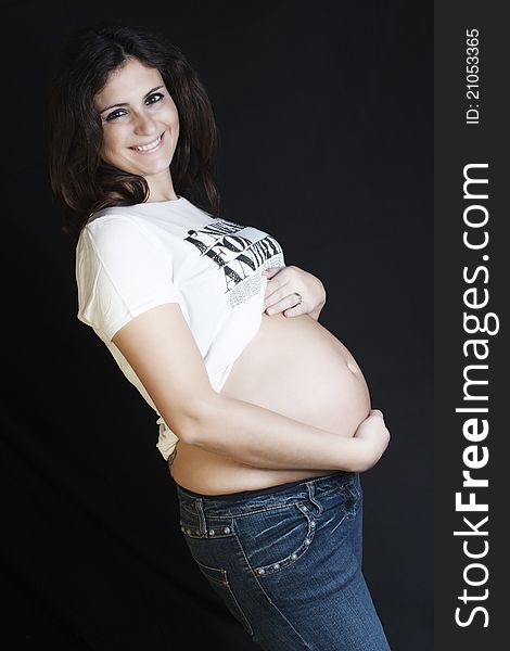 Pregnant woman with a jeans and white T-shirt standing on a black background. Pregnant woman with a jeans and white T-shirt standing on a black background