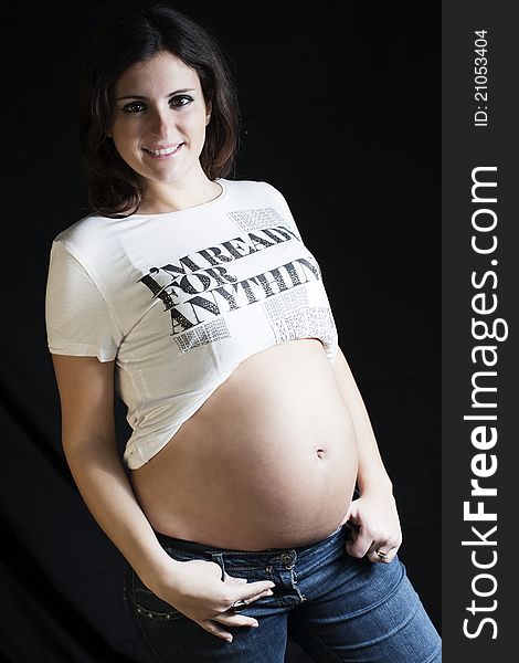 Pregnant woman with a jeans and white T-shirt standing on a black background. Pregnant woman with a jeans and white T-shirt standing on a black background