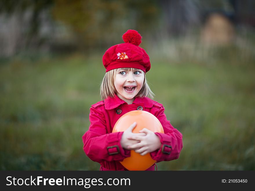 Girl with surprised face, smilling, wears in a red cap and red coat, holding orange balloon. Girl with surprised face, smilling, wears in a red cap and red coat, holding orange balloon