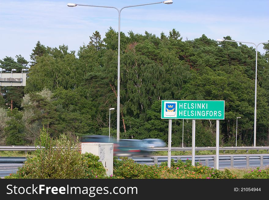Helsinki city limit sign along a busy motorway with blurred cars in background.
