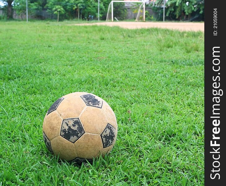 An old soccer ball on ground, goal is the background. An old soccer ball on ground, goal is the background