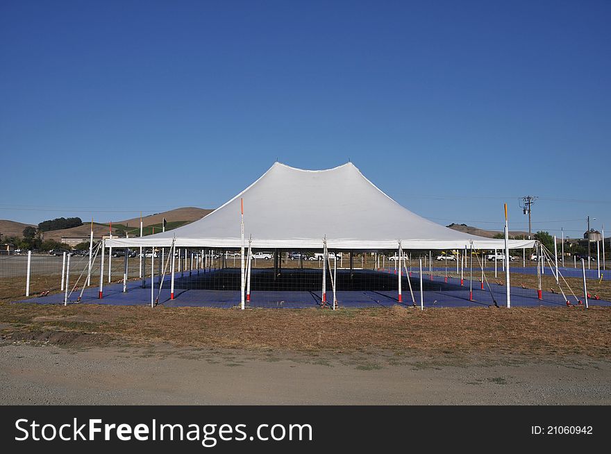 A white tent covers an empty space with hills in the background. A white tent covers an empty space with hills in the background