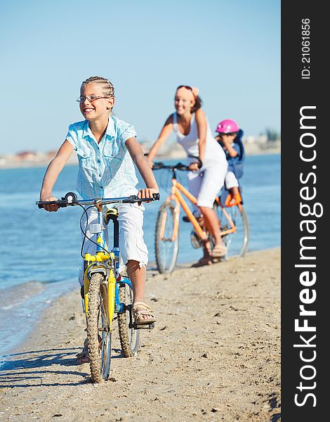 Cute girl with her mother and brother ride bikes along the beach. Focus on girl. Vertical view