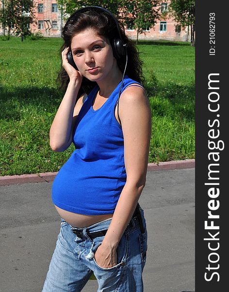 Pregnant woman goes into the headphone, outdoor