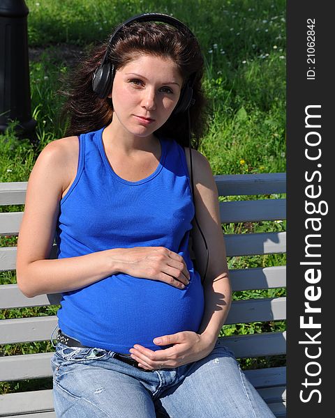 Happy pregnant woman sitting on a bench and hugged her belly
