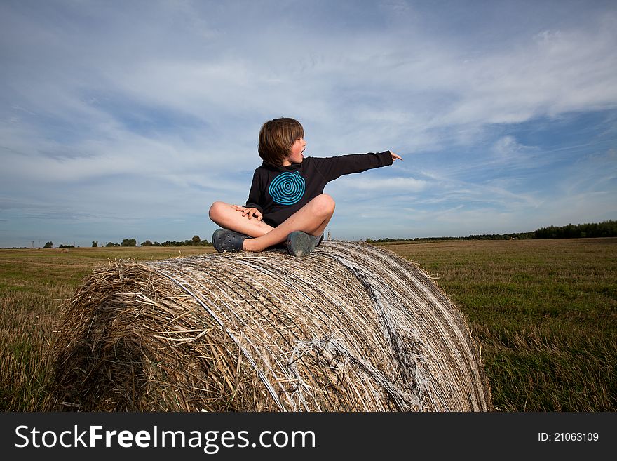 Boy sitting on hay bales, pointing on something. Boy sitting on hay bales, pointing on something