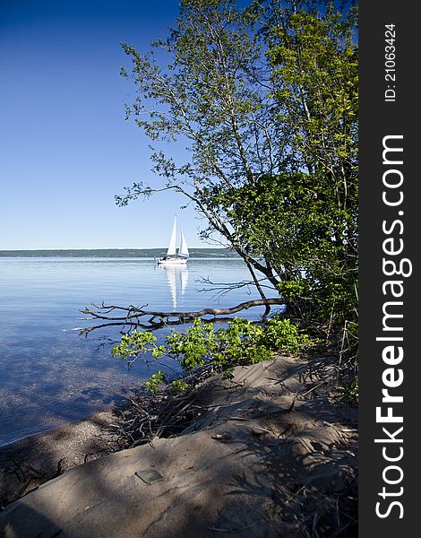 Sailboat on calm water with reflection in water surface. Green vegetation in front. Sailboat on calm water with reflection in water surface. Green vegetation in front.