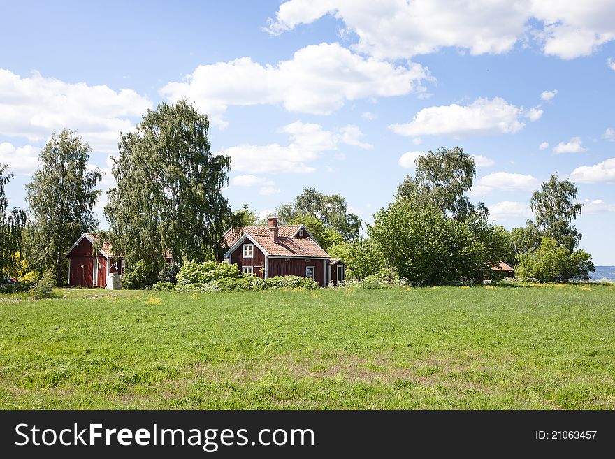 Small red house in a green field. House is surrounded by beautiful trees. Small red house in a green field. House is surrounded by beautiful trees.