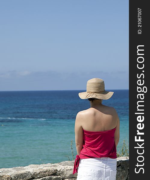 A woman in a straw hat looking out to sea.