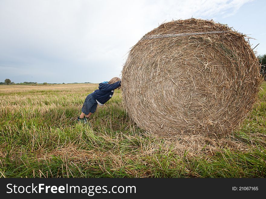 A small boy pushing huge bales of hay. A small boy pushing huge bales of hay