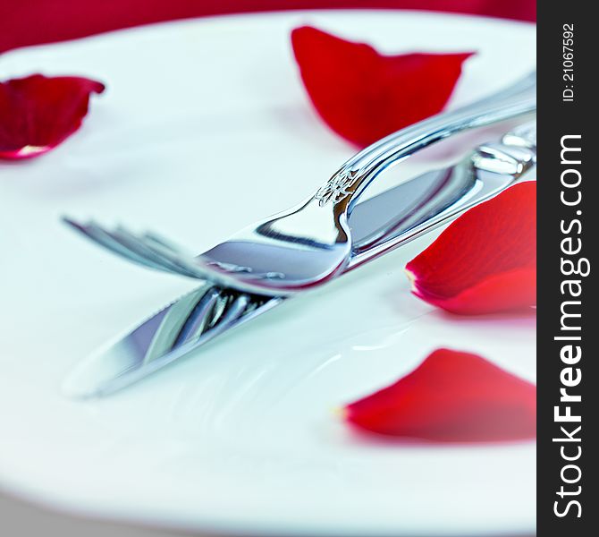 Closeup of fork and table knife with red rose petals. Closeup of fork and table knife with red rose petals