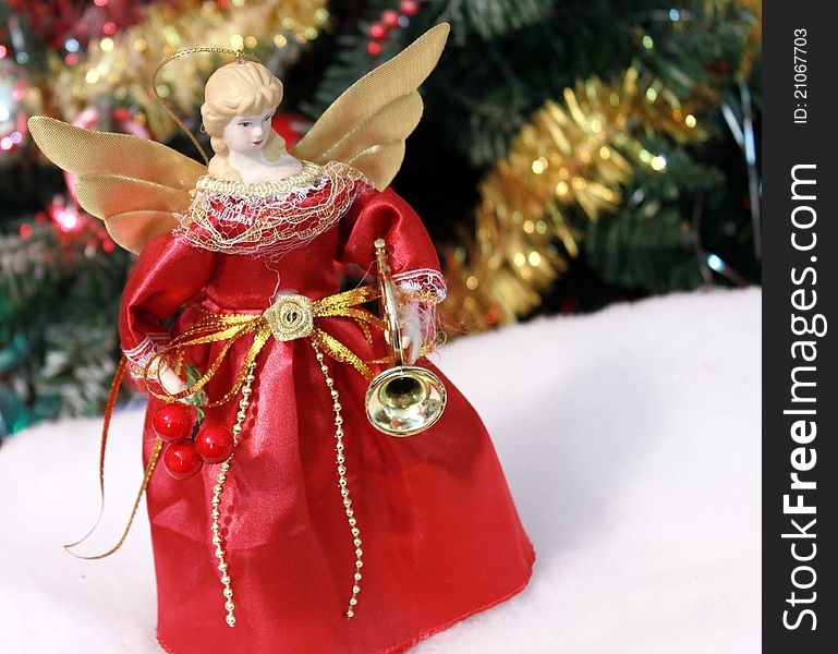 Christmas angel decoration under tree in red dress and gold wings