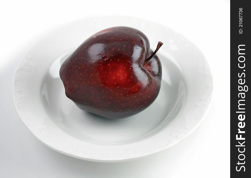 Dark red apple over white plate on white background. Dark red apple over white plate on white background