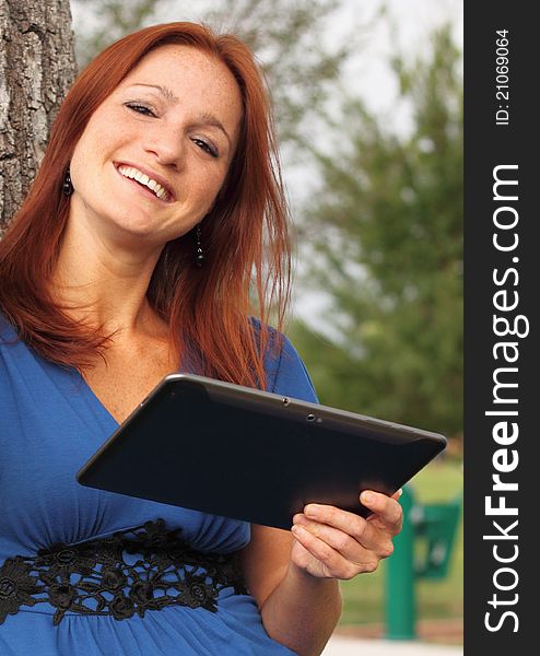 Pretty woman using a tablet leaning against a tree at the park. Pretty woman using a tablet leaning against a tree at the park