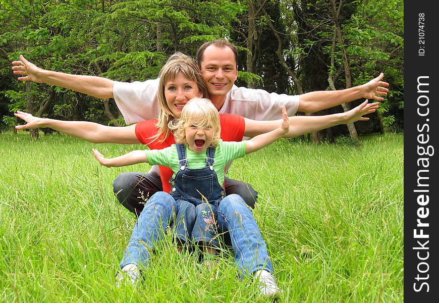 Happy family with little girl sits on meadow and lauthing