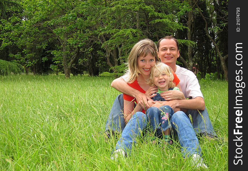 Happy family with little girl sits on meadow and lauthing