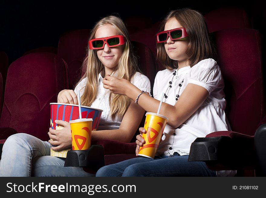 Two girls look three-dimensional cinema, sitting in the glasses, eat popcorn, drink drink. Two girls look three-dimensional cinema, sitting in the glasses, eat popcorn, drink drink