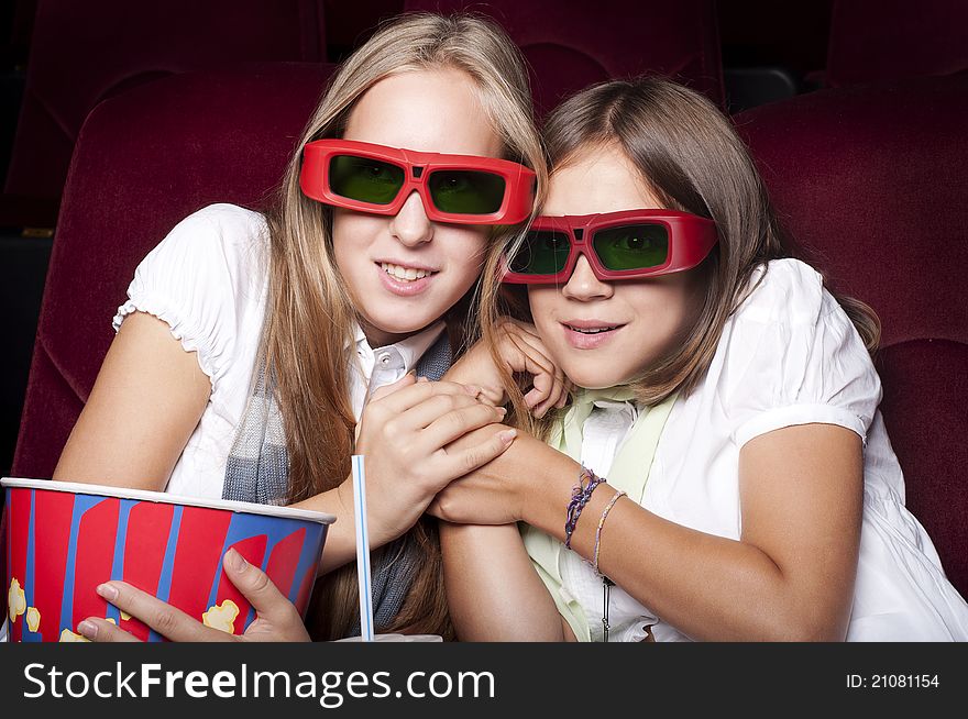 Two girls look three-dimensional cinema, sitting in the glasses, eat popcorn, drink drink. Two girls look three-dimensional cinema, sitting in the glasses, eat popcorn, drink drink