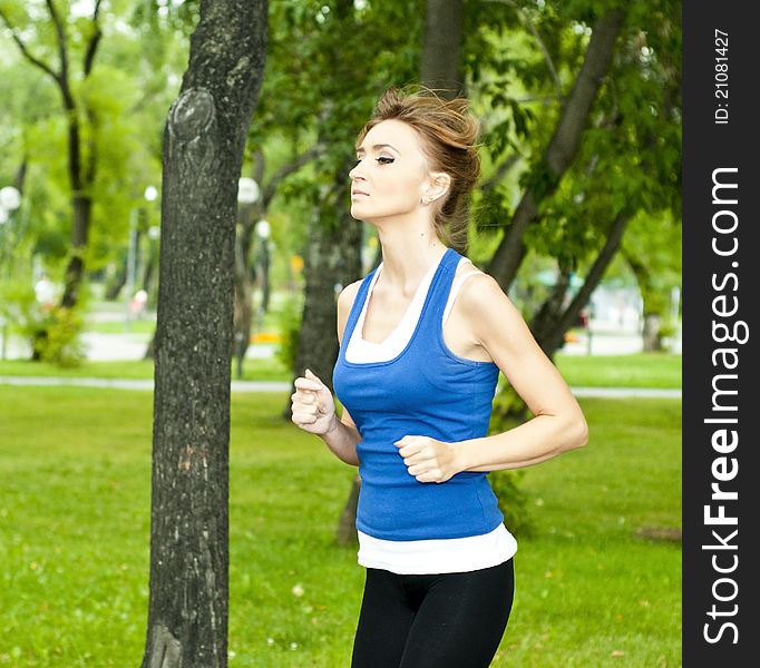 Young woman jogging in the park in summer, trees and grass background