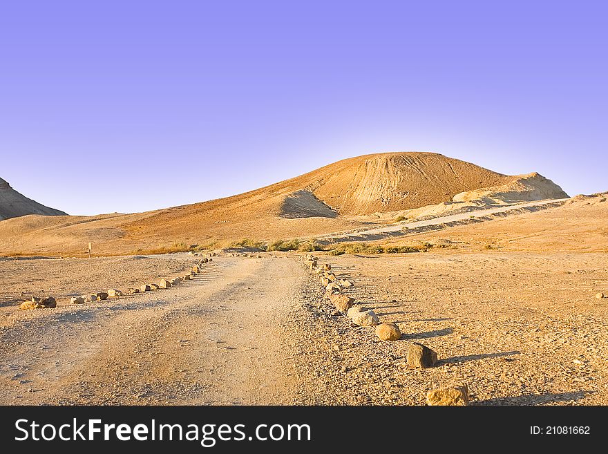 A stone-boarded track leading to a sight point in desert faces a golden hill and blue skies. A stone-boarded track leading to a sight point in desert faces a golden hill and blue skies.