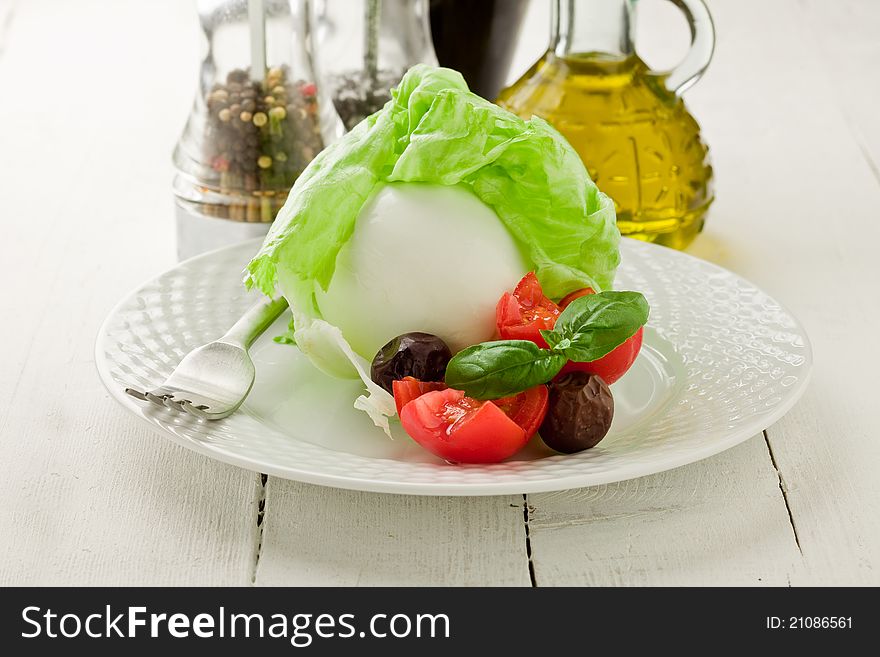 Delicious buffalo mozzarella with wrapped lettuce and tomatoes on wooden table