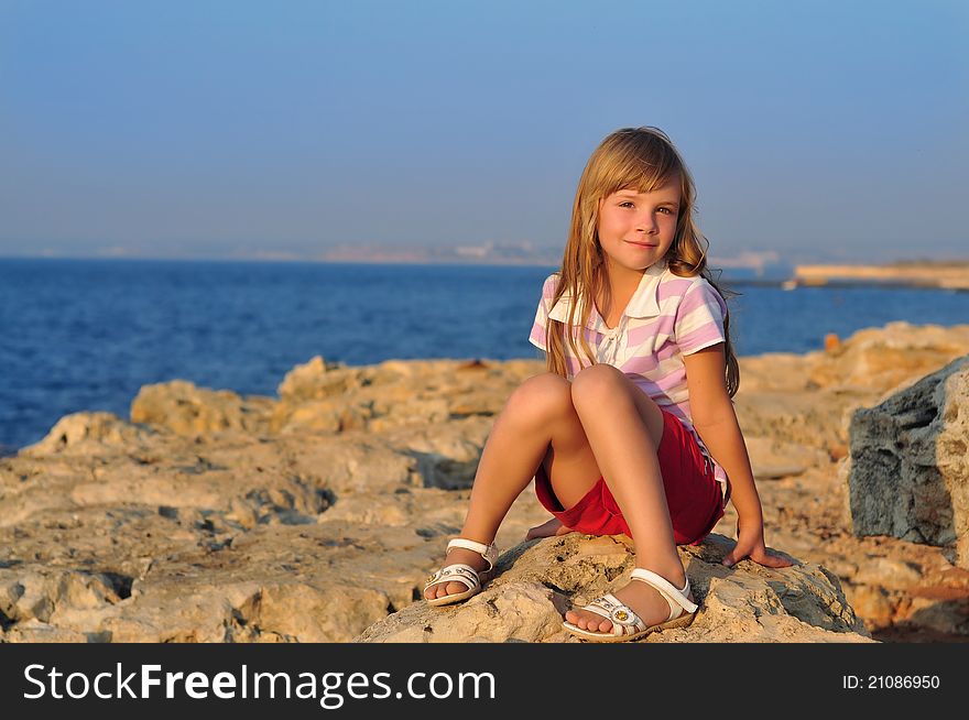 A girl sitting on rocks by the sea at sunset. A girl sitting on rocks by the sea at sunset