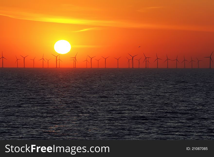 Silhouette of wind power stations over the sea at sunset