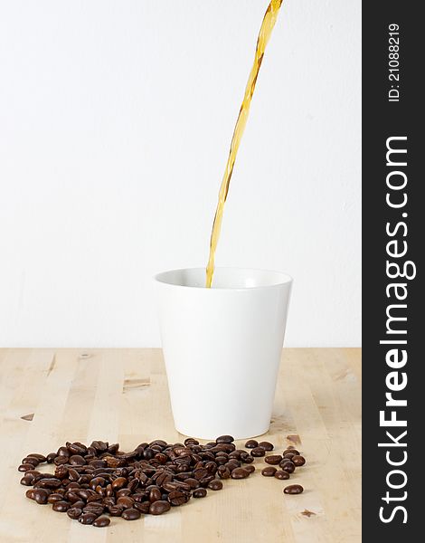 Picture of coffee beans and a white cup on a table. Coffee being poured in the cup. Picture of coffee beans and a white cup on a table. Coffee being poured in the cup