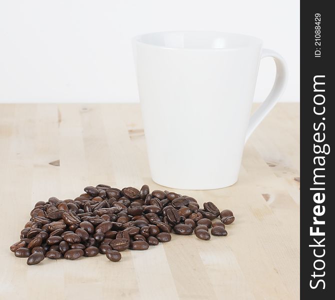 Picture of coffee beans and a white cup on a table. Picture of coffee beans and a white cup on a table