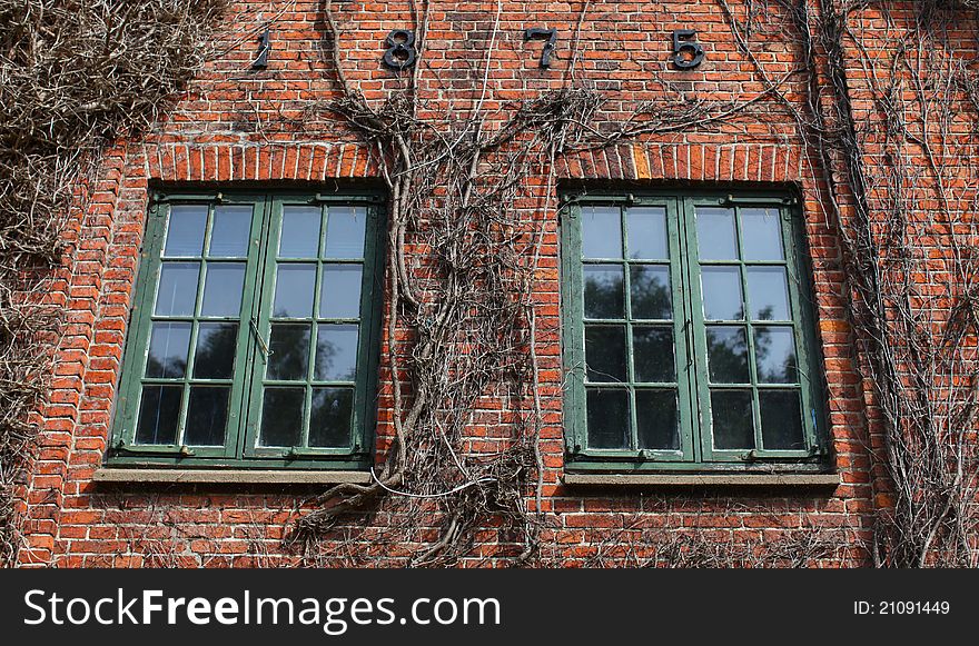 Brick house detail with two window and vines climbing the wall. Brick house detail with two window and vines climbing the wall.