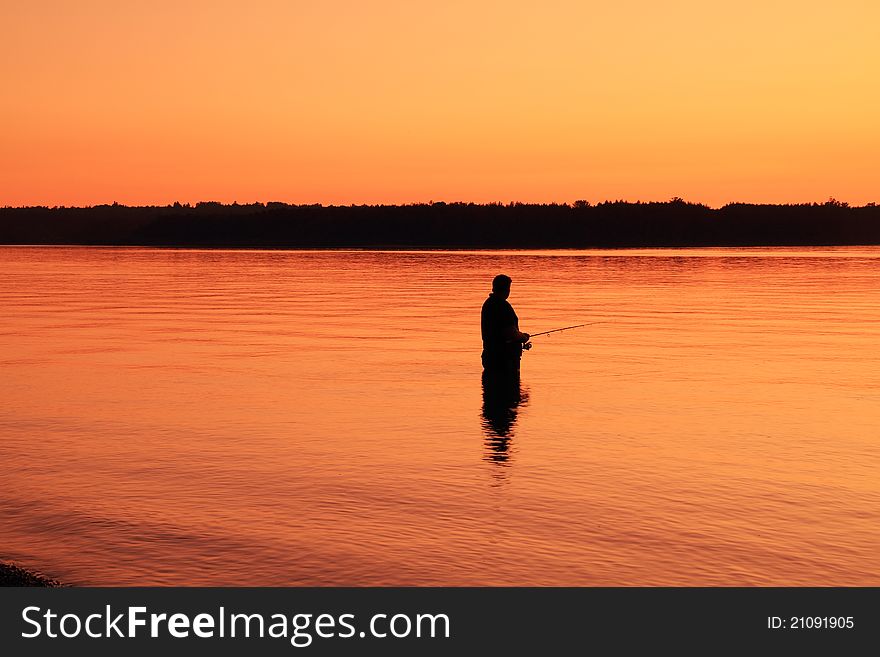 A lone river fisherman is silhouetted against a golden orange sunset. A lone river fisherman is silhouetted against a golden orange sunset.
