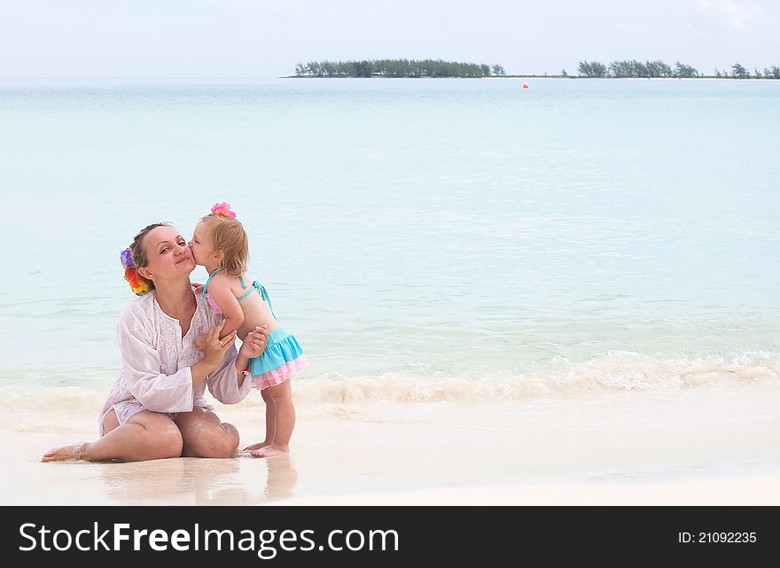 A baby girl is kissing her mother on the beach of the ocean on vacation
