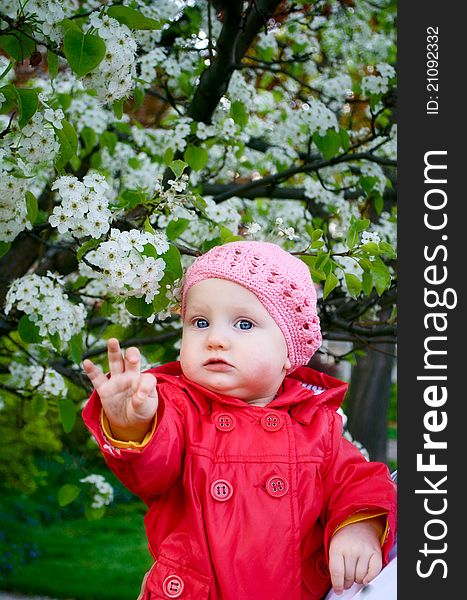 A baby girl in the garden next to blossom tree