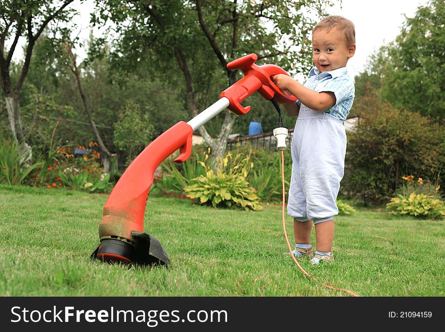 Young baby boy with trimmer in garden