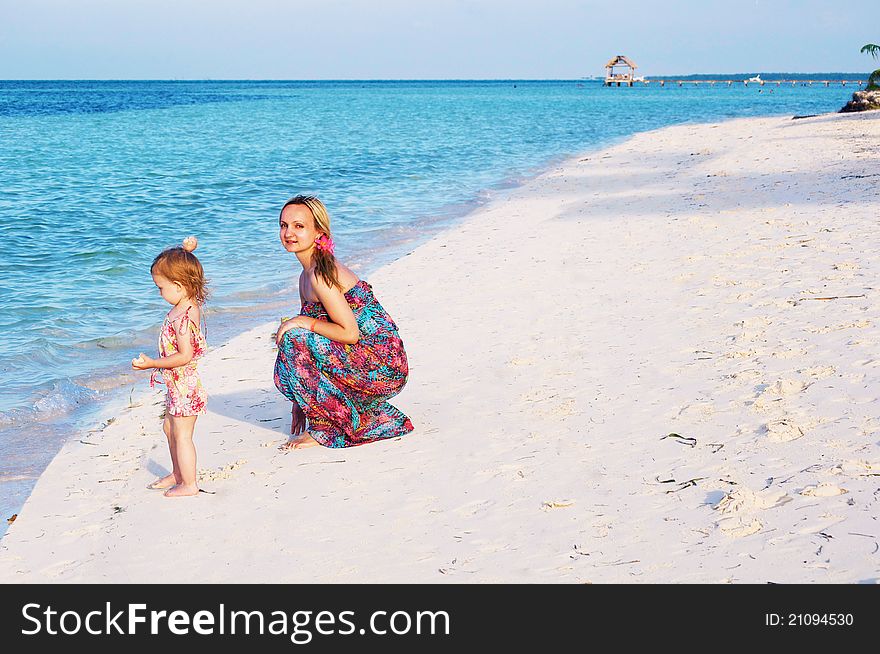 A young mother is playing with a baby girl on the beach of the ocean. A young mother is playing with a baby girl on the beach of the ocean