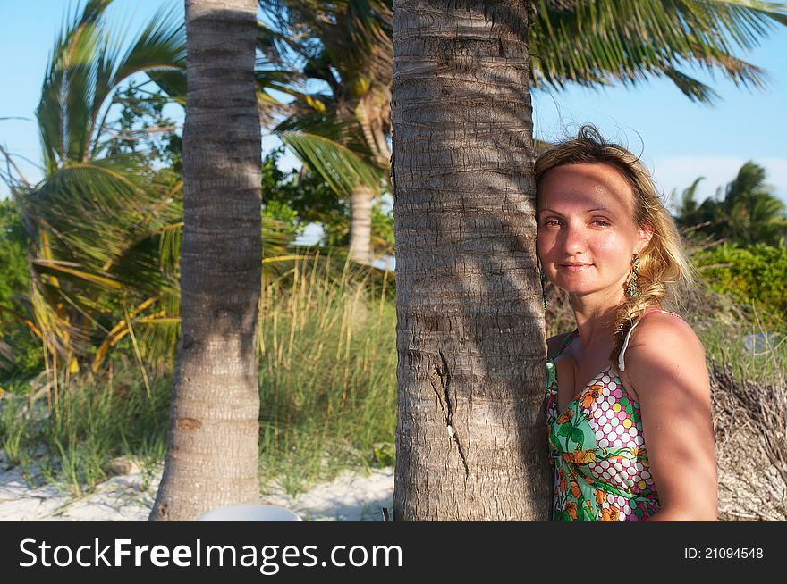 A young woman is standing next to the palm tree smiling. A young woman is standing next to the palm tree smiling