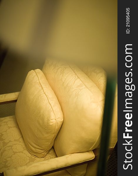 A plush gold coloured armchair and cushion with ornate emroidery. A plush gold coloured armchair and cushion with ornate emroidery