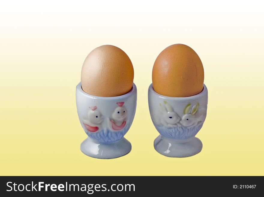 Two eggs in novelty egg cups on a yellow background. Two eggs in novelty egg cups on a yellow background