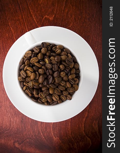 Coffee cup full of coffee beans on dark shiny wood. Coffee cup full of coffee beans on dark shiny wood.