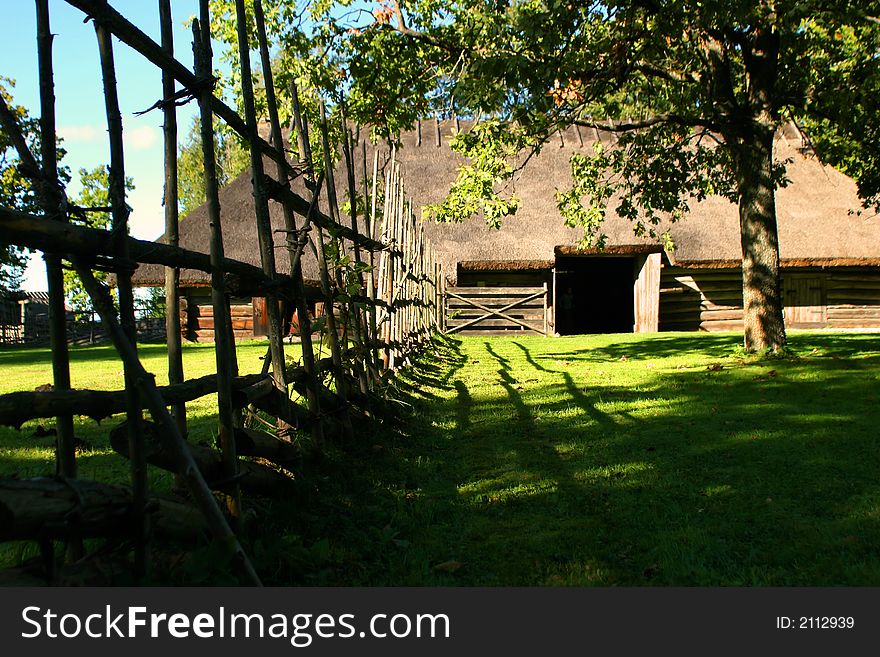 Old curve fence and greater log hut with a straw roof. Old curve fence and greater log hut with a straw roof