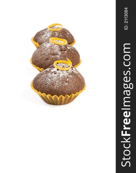 Vertical row of three chocolate muffins with lemon peel on the top on white background