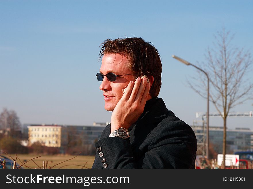 A young business man is talking to someone on his mobile. He is outside, enjoying a sunny day. A young business man is talking to someone on his mobile. He is outside, enjoying a sunny day.