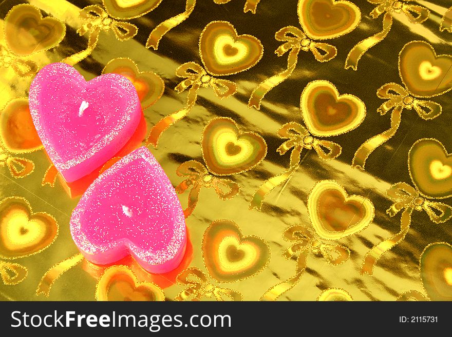 Two candles in the form of hearts on a golden background