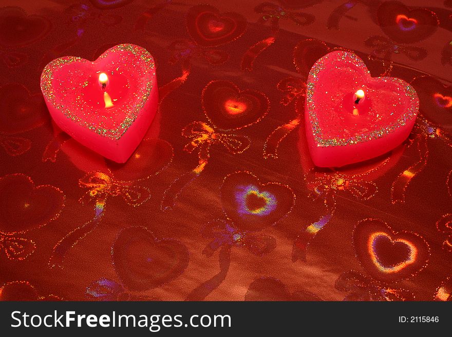 Two candles in the form of hearts on a red background