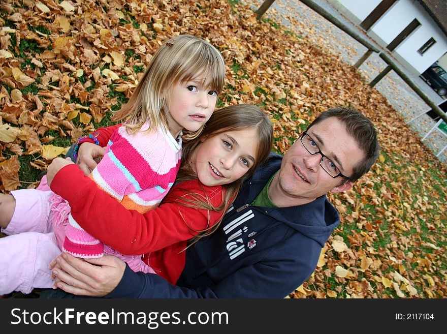 Father with his two daughters sitting in a park in autum leaves. Father with his two daughters sitting in a park in autum leaves