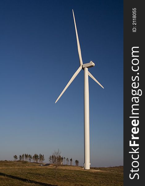 Aerogenerator with a set of trees on the horizon over a blue sky. Aerogenerator with a set of trees on the horizon over a blue sky